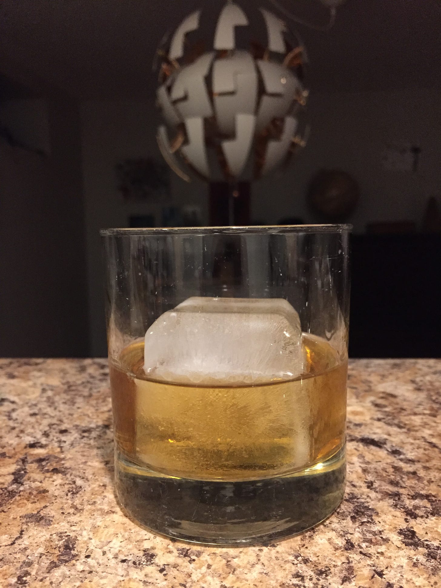 A rocks glass with a large square ice cube, half out of the drink