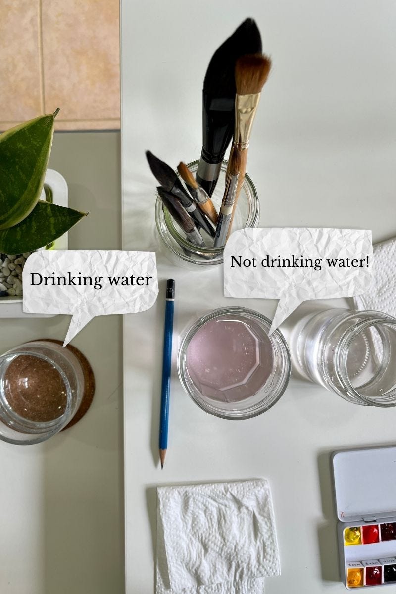 Image: top view photo of watercolour brushes, two bottles with water for the watercolour brushes, kitchen towel for drying the brushes, and a glass of water. The wording on the photo is “For drinking.” (Pointing to the glass of water). “Not for drinking.” (Pointing to the two bottles with water to wash the watercolour brushes)