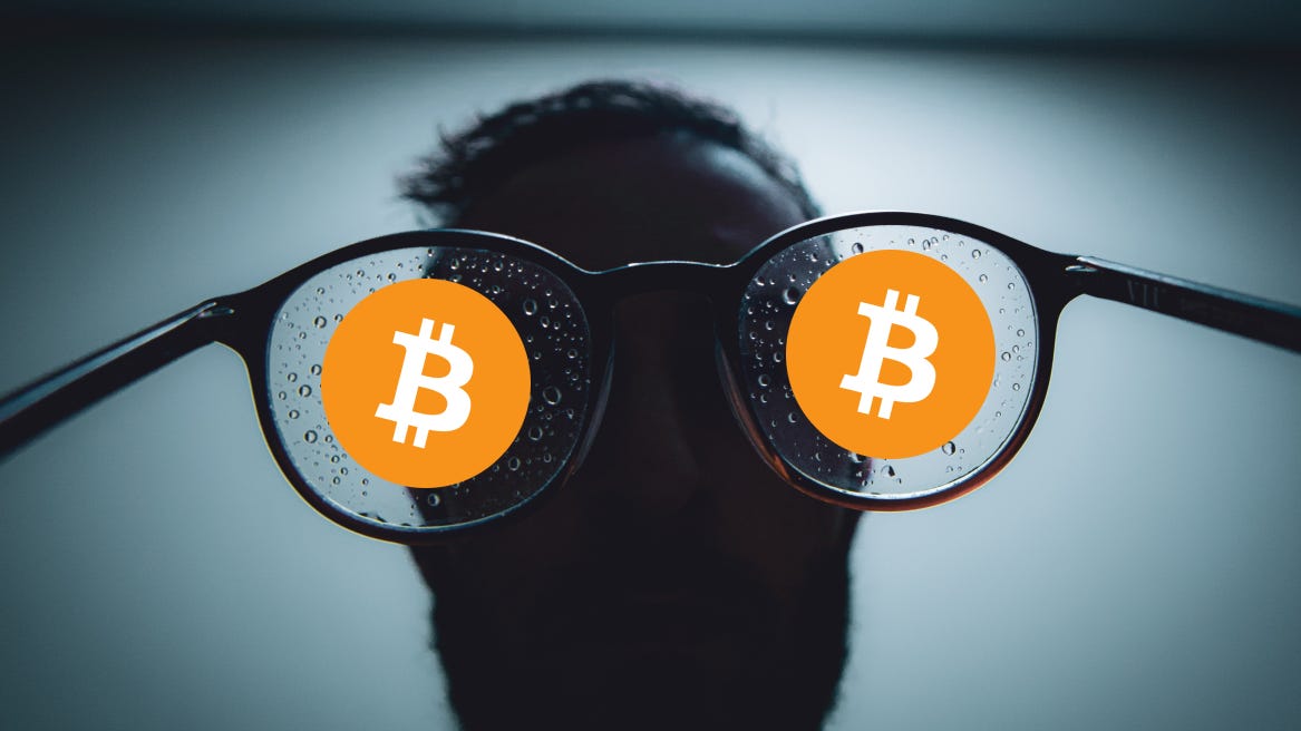 Bitcoin glasses with two logos and man in background in dark room