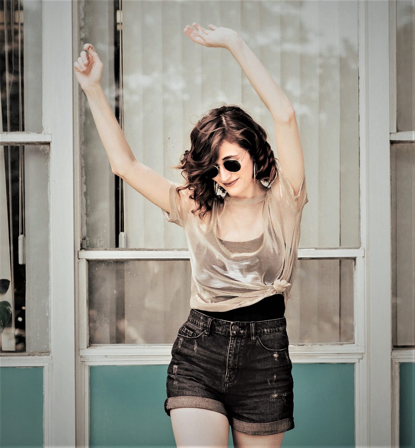 happy girl with brown hair wearing dark glasses waving her arms in the air