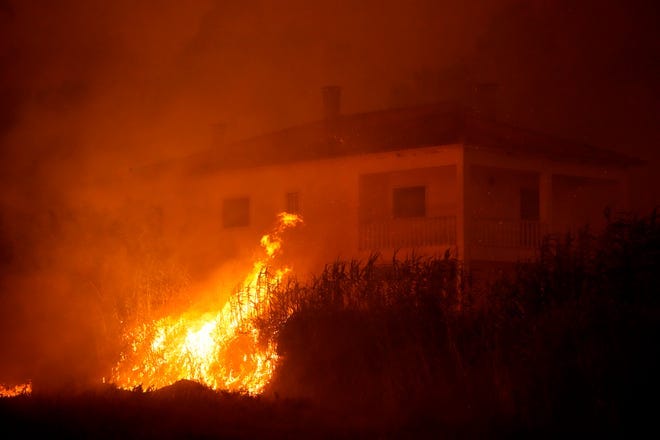 A forest fire reaches an empty house as smoke darkens the sky in the village of Bemposta, near Ansiao, central Portugal, Wednesday, July 13, 2022. Thousands of firefighters in Portugal continue to battle fires all over the country that forced the evacuation of dozens of people from their homes.