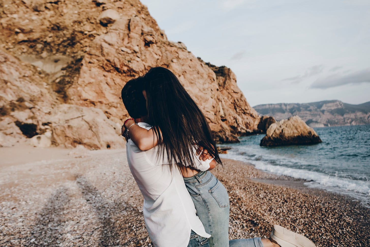 A dark-haired couple embrace on a beach.