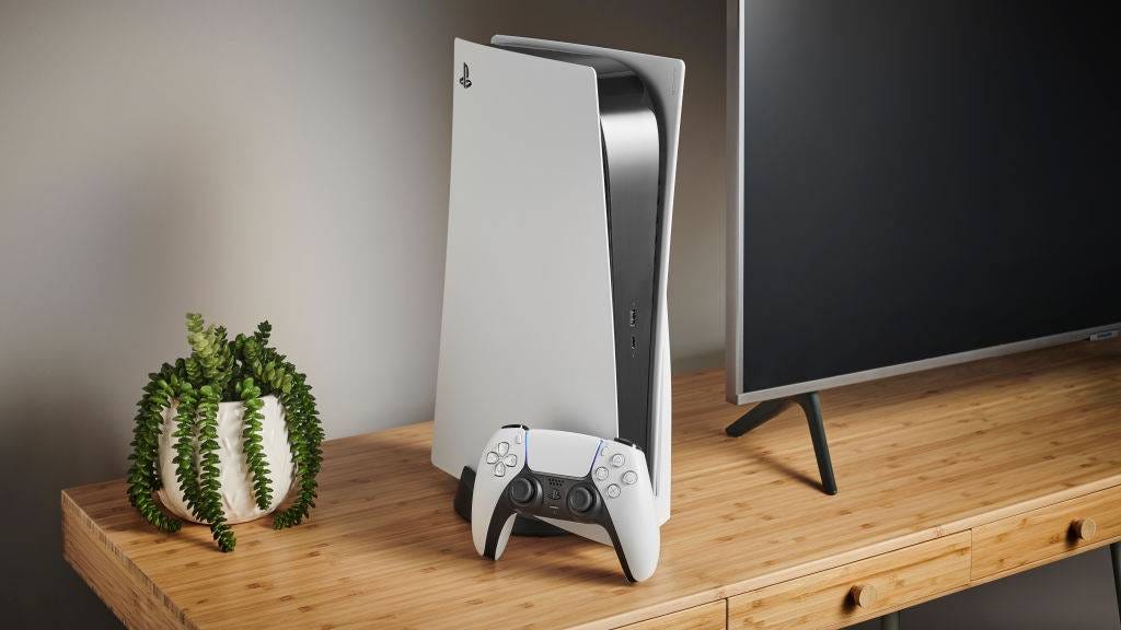 PS5 standing vertically on a wooden desk next to a TV and potted plant