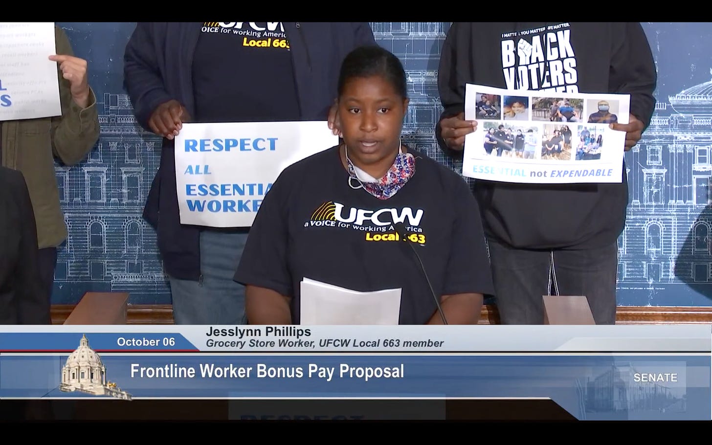 A black woman in a black tee shirt with white text reading UFCW Local 663 stands behind a podium, speaking