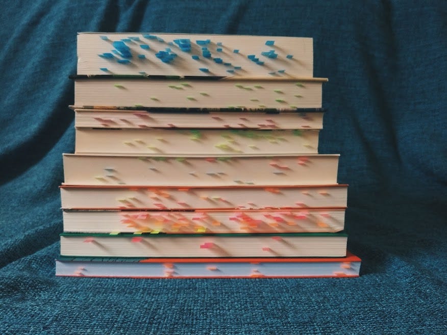 Uma pilha de livros, com post-its marcando trechos do texto.