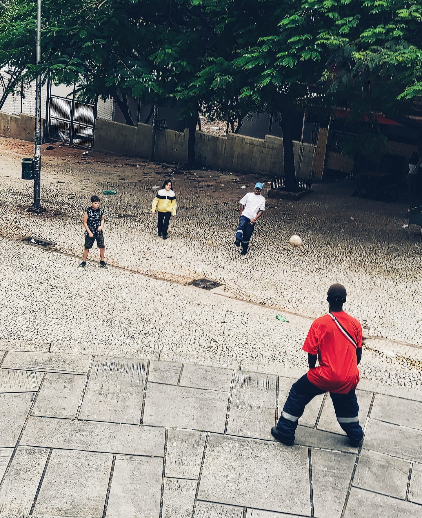 Duas crianças e dois adultos, em uniforme de trabalho, jogam bola na Ladeira da Memória, no Anhangabaú