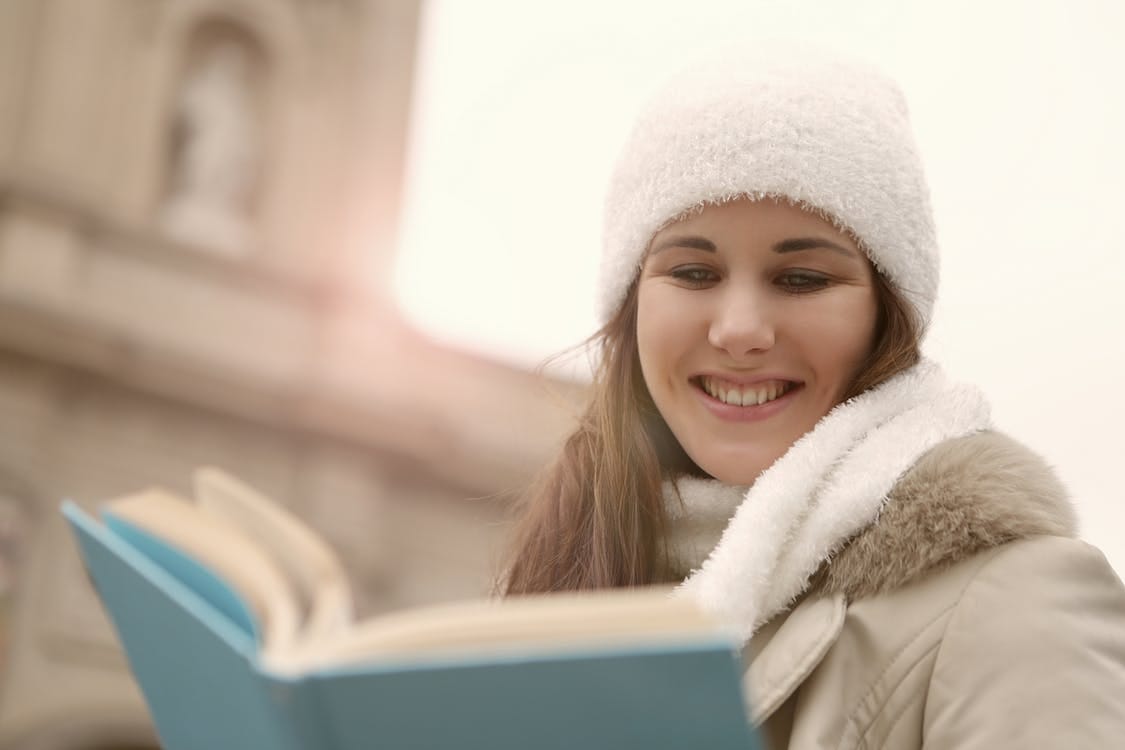 Free A Happy Woman in White Knitted Beanie Reading a Book Stock Photo