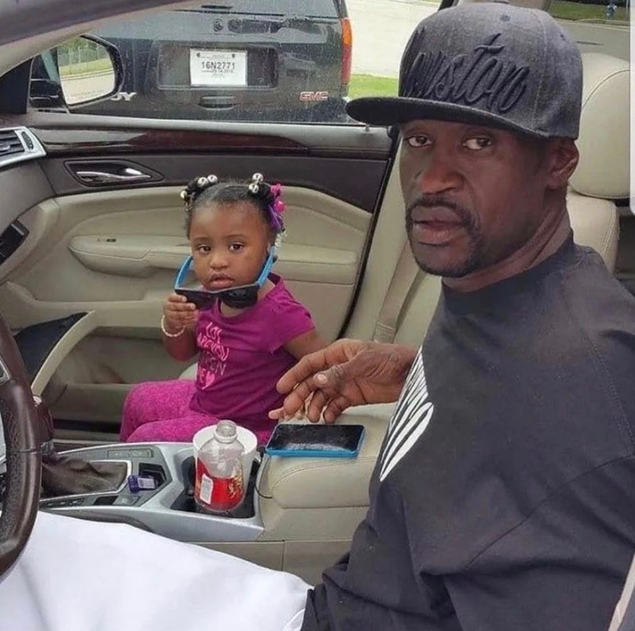 George Floyd in car with black hat and black shirt on next to his daughter Gianna with sunglasses on