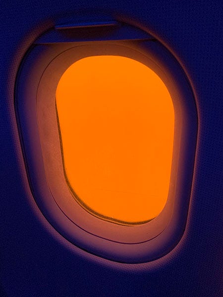 A photo of a window on an airplane where the wall is dark purple and the window is only orange. 