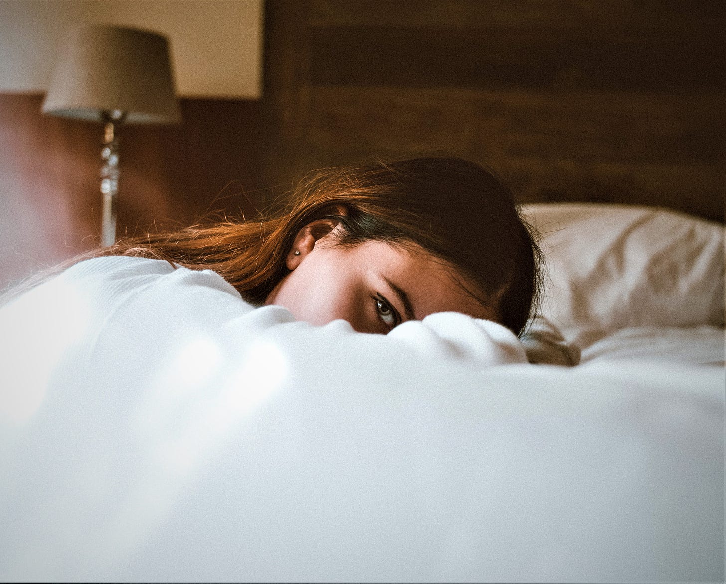 girl with brown hair laying down on bed arm covering face