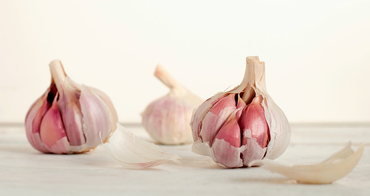 Three heads of garlic, two half-peeled, on a white surface