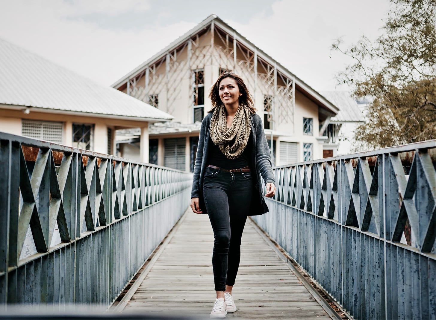 smiling girl with brown hair wearing sweater walking across wooden bridge