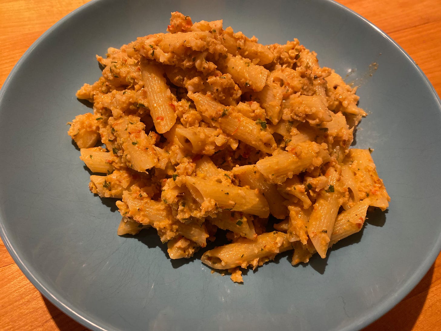 A pile of penne tossed with cauliflower pesto in a shallow blue blue.