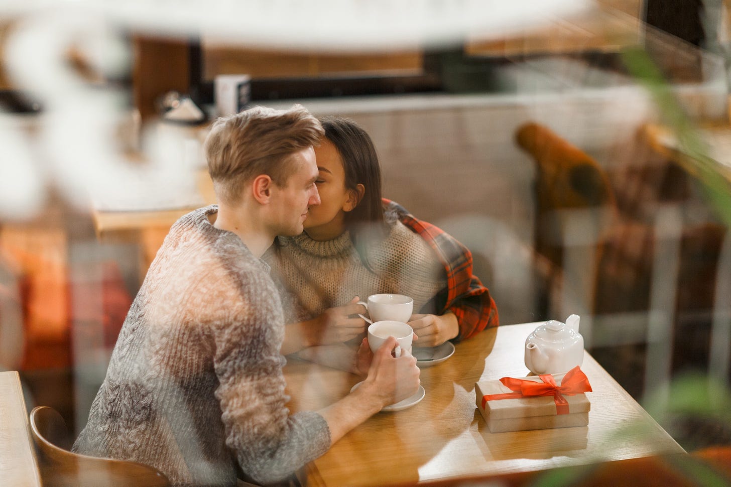 A man and a woman lean into one another flirtaciously in a cafe.