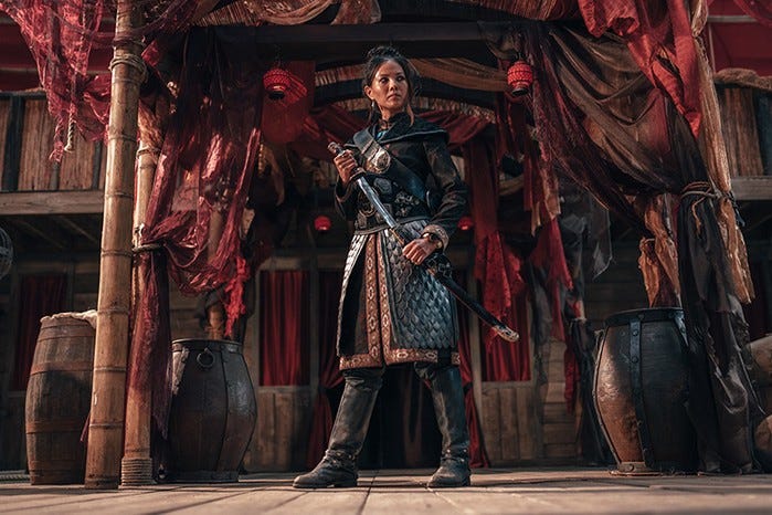 This image shows the character of Madam Ching (played by Crystal Yu), 19th-Century China's so-called "pirate queen," standing on the deck of her ship draping her sword across her body. The sword remains in its scabbard. This image shows the character of Madam Ching (played by Crystal Yu), 19th-Century China's so-called "pirate queen," standing on the deck of her ship draping her sword across her body. The sword remains in its scabbard.