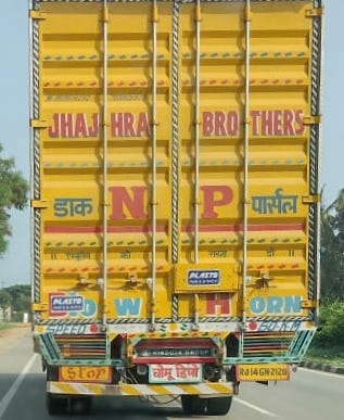 Image of the back of a truck. it is painted yellow and has devnagri script on it. The bottom says in hindi: chomu depot
