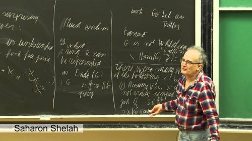 A picture of Saharon Shelah standing in front of a blackboard.