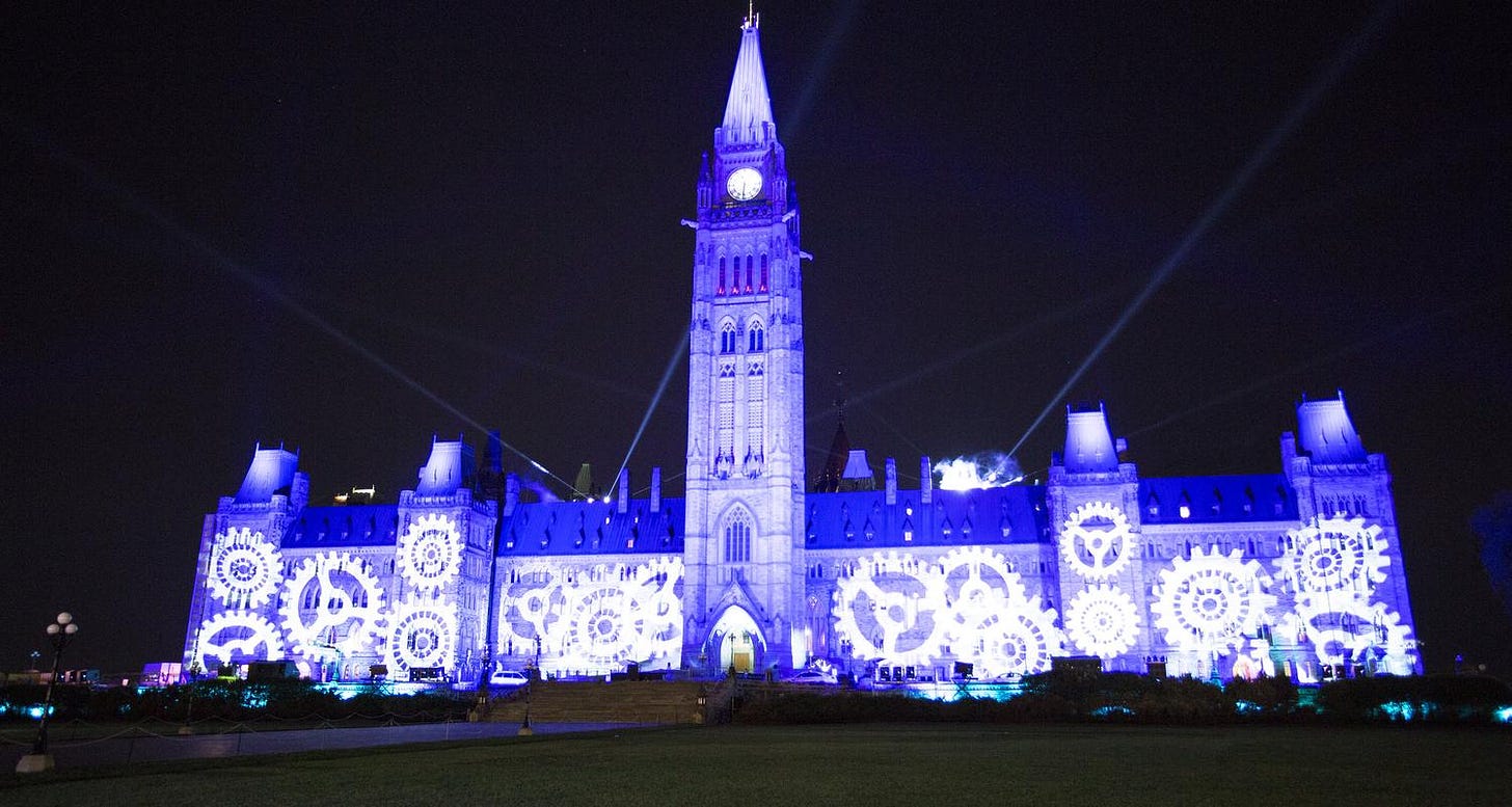 Centre Block illuminated in blue light, with the image of gears as part of the Northern Lights sound and light show.