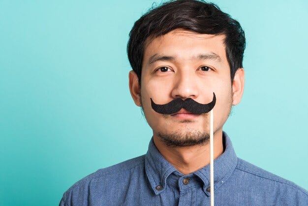 Handsome man posing he holding a funny mustache card or vintage fake moustaches on his mouth Premium Photo