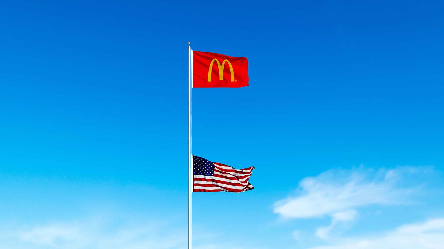 An illustration of a McDonald’s flag flying above a US Flag. The US flag is at half mast.