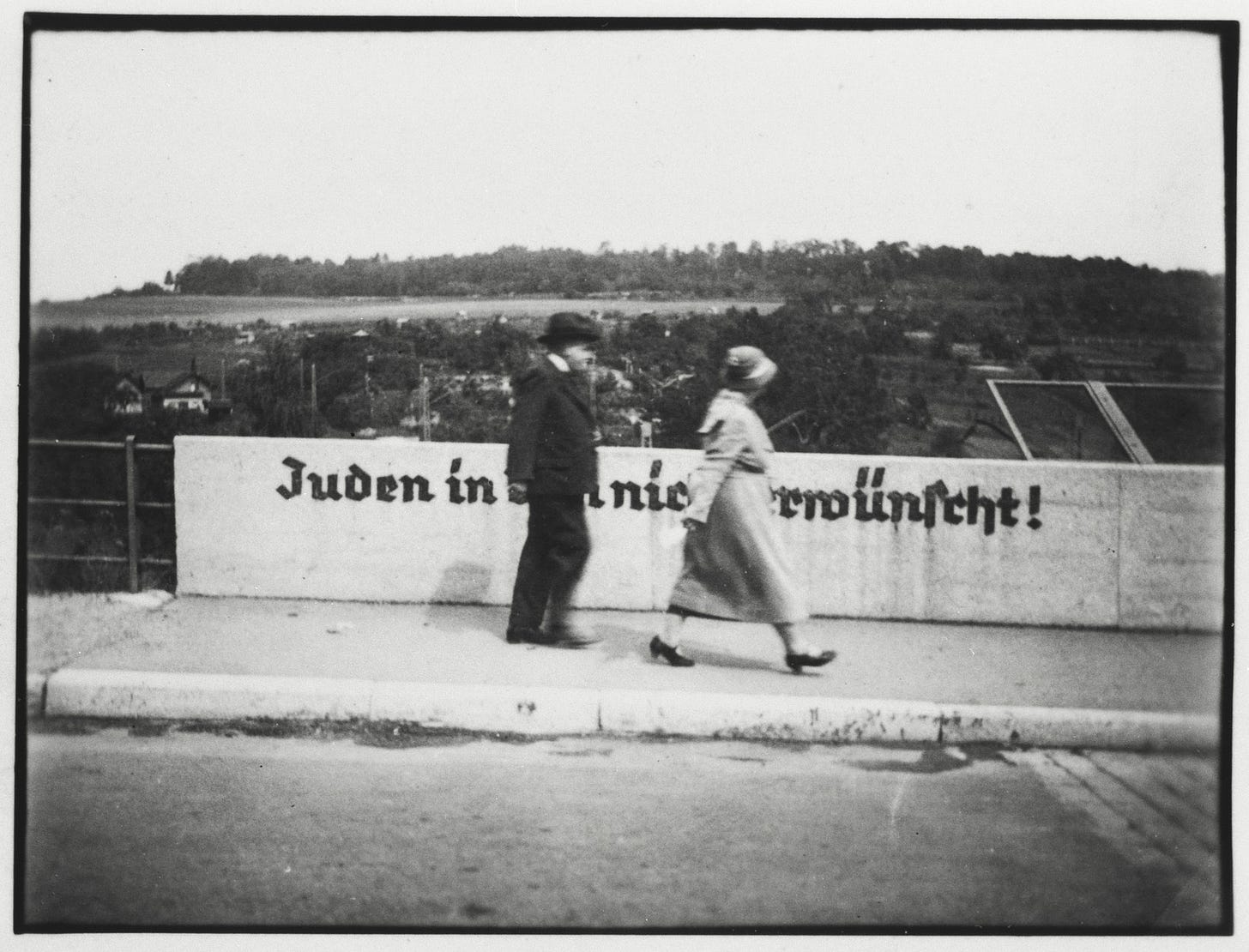 A Jewish gentleman and his daughter cross the Stuttgarter Strasse bridge in Ulm that is painted with the sign "Jews are not desireable in Ulm".