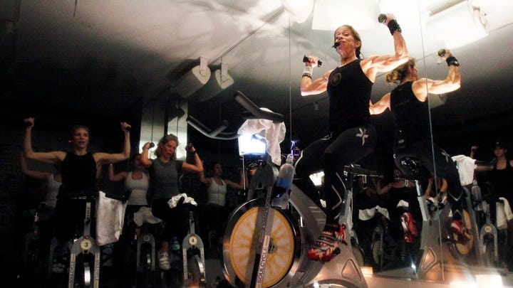 A woman lifts weights while riding a SoulCycle stationary bicycle.