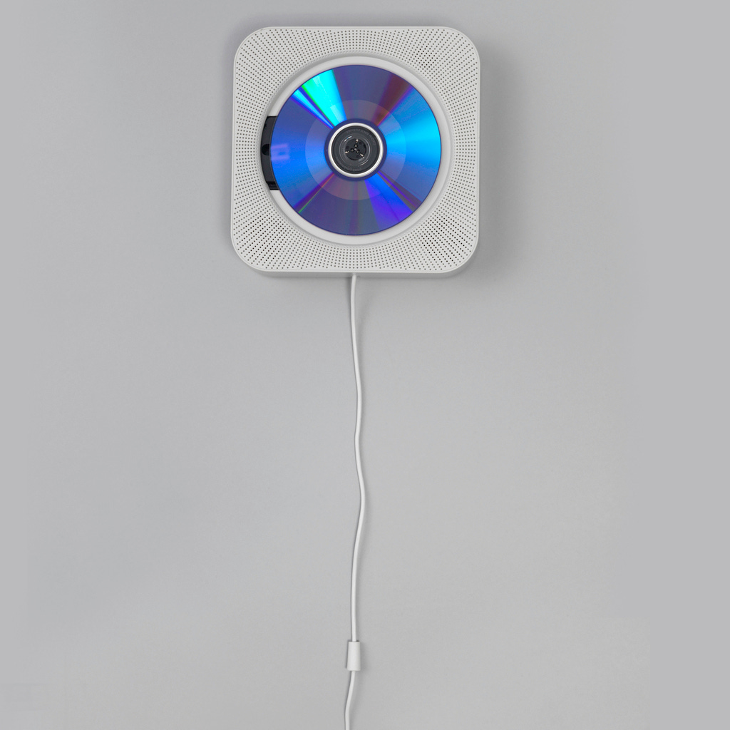 White plastic square body with rounded corners; face pierced for speaker; large central circular indentation with reader having center spindle to recieve and play CD; white power cord hanging from center bottom acts as on/off pull switch.