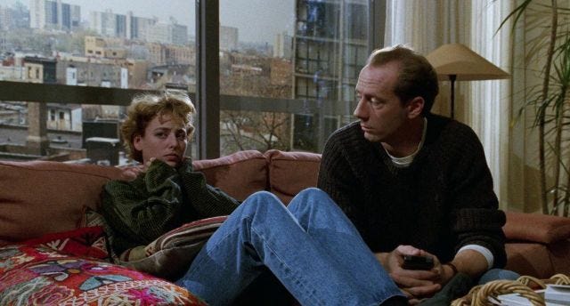 Virginia Madsen, looks scared, sits on the sofa next to a man who looks at her 