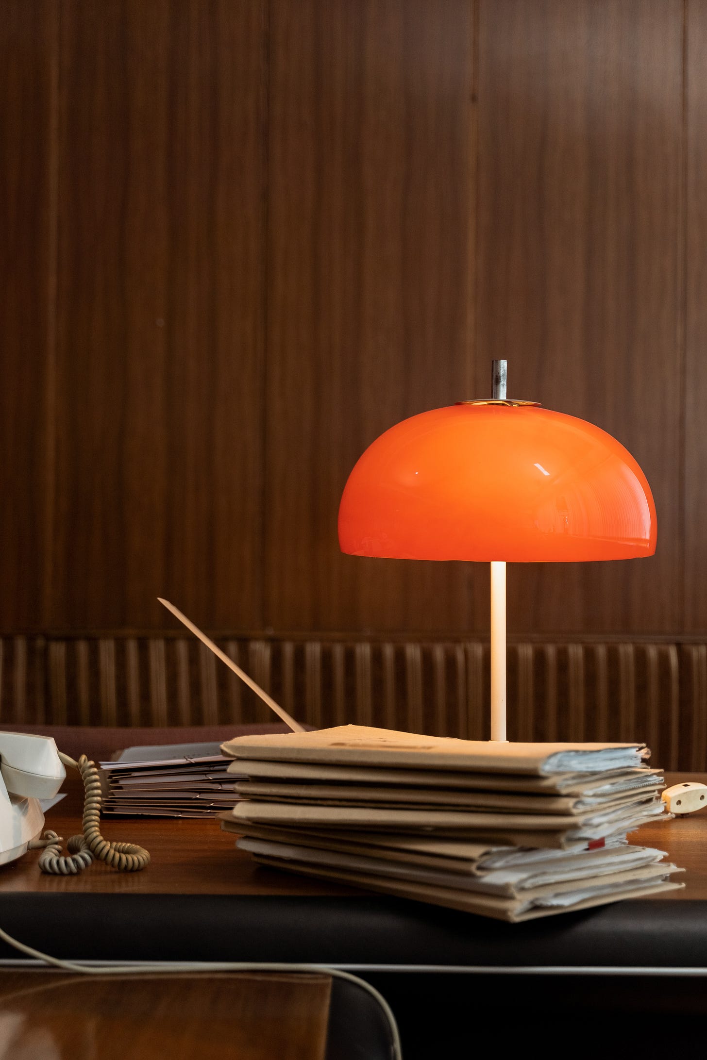 Medical files sit on a wooden desk with a bright orange lamp turned on, shining light on the table.
