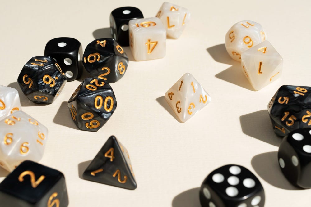 A number of black and pearl dice, of different types, resting on a cream coloured surface