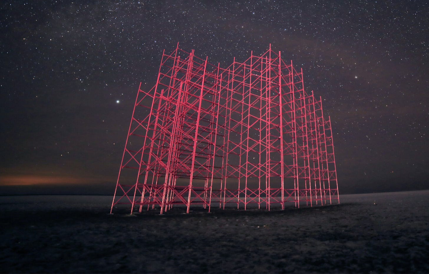 A 40-ft hot pink scaffolding lit up at night with a starry black sky behind it.