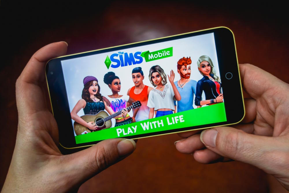 Close up of hand of person playing The Sims Mobile game apllication.