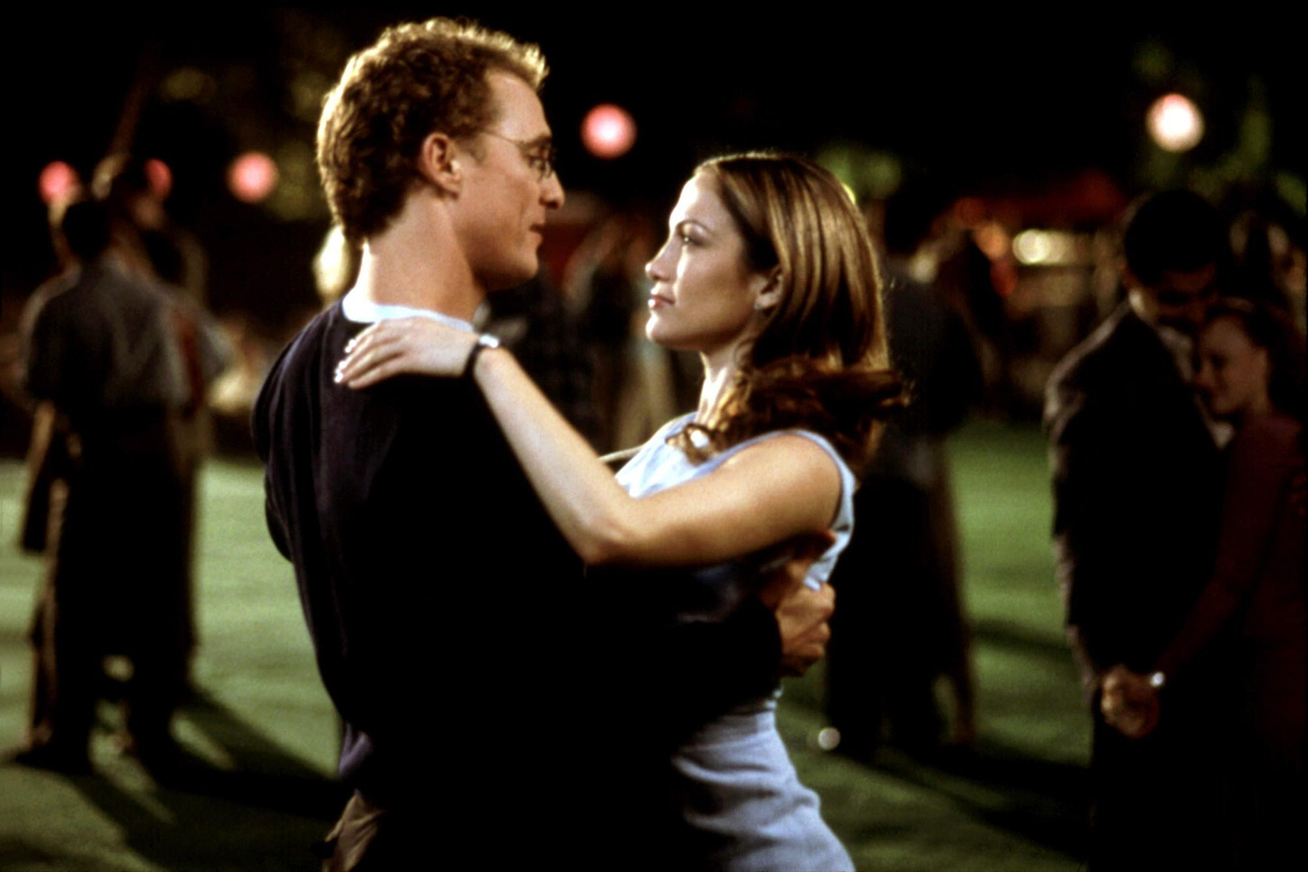 A close-up of McCaunaghey and Lopez dancing in the park at night.