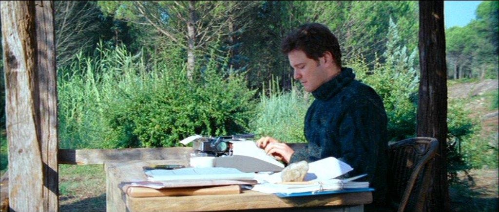 Colin Firth in Love Actually typing on a typewriter at a desk outside.