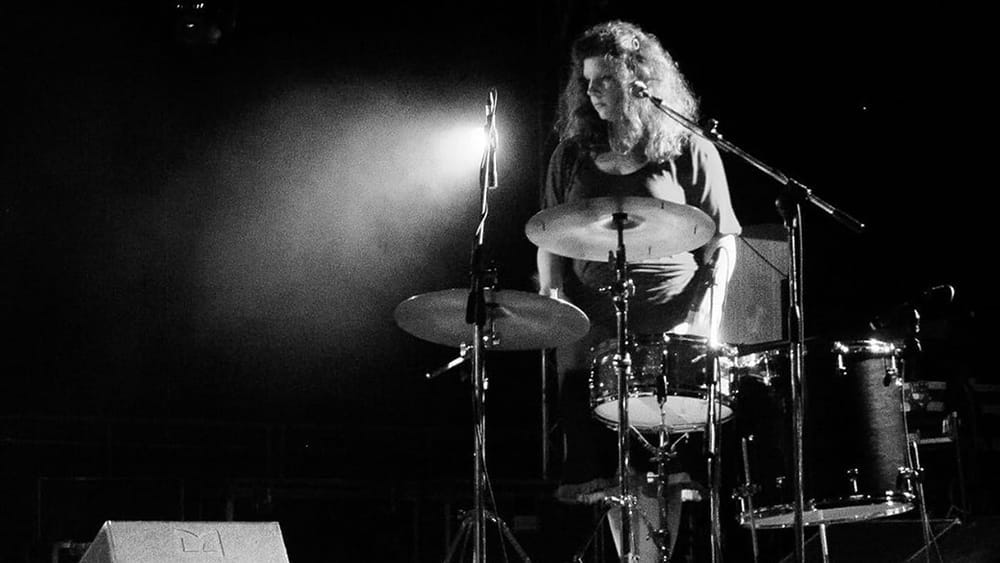 Black and white photo of Low's Mimi Parker standing at her drum kit