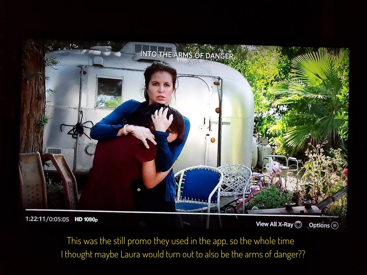 Laura cradling Jenny in front of an Airstream trailer with a big fake spider dangling from it, captioned "This was the still promo they used in the app, so the whole time I thought maybe Laura would turn out to also be the arms of danger??"