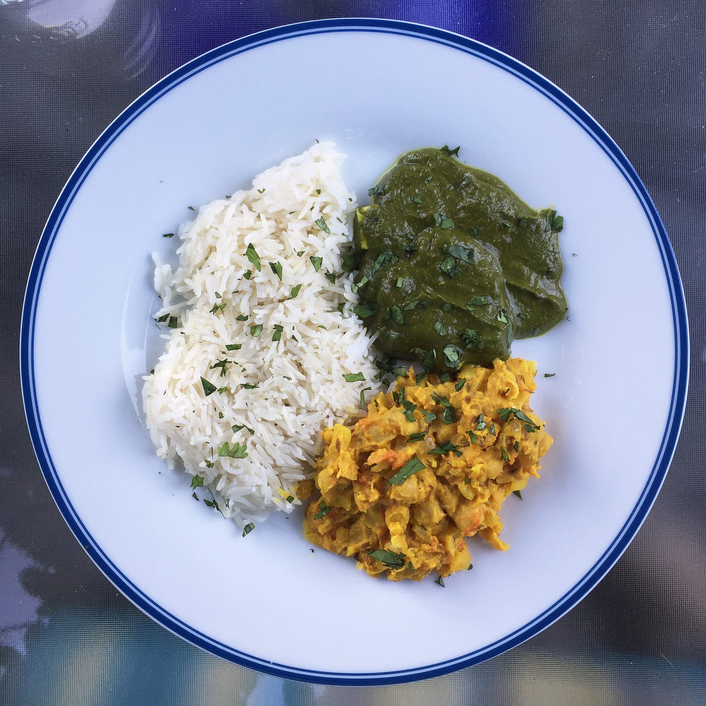 a white plate of basmati rice, dark green saag paneer, and yellow chana masala in each third of the plate. Cilantro is scattered over the top.