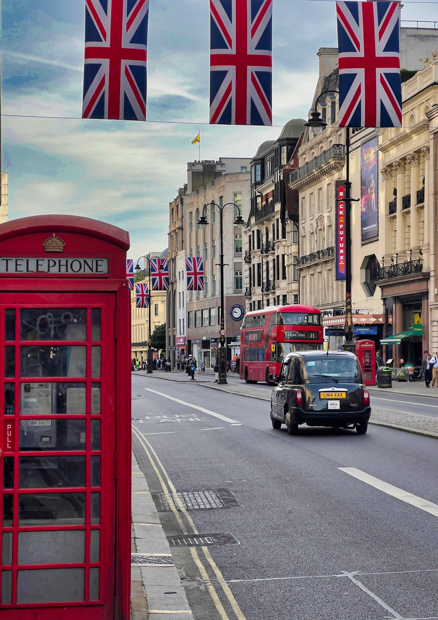 London street scene with red telephone box in the forefront left, double decker bus on the right, buildings and union flags hung across the street