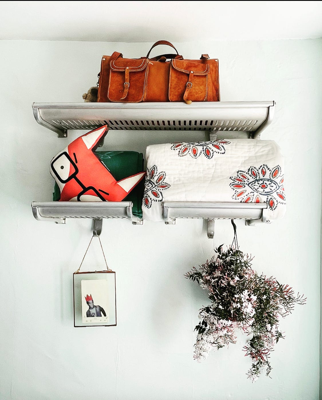 Photo of shelves with a bag, cushions and quilt and a jasmine plant hanging from them