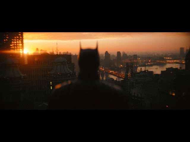 Batman in foreground (blurry) overlooking the whole of Gotham as the sun rises.