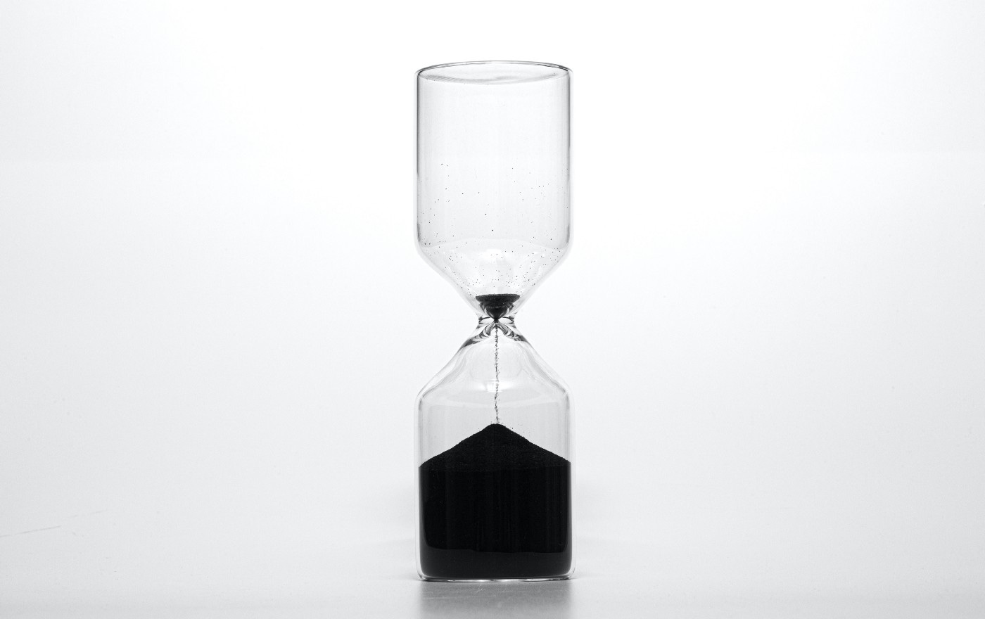 A hourglass is shown with most of the sand on the bottom. Only a little bit of sand is at the top with it flowing into the bottom.