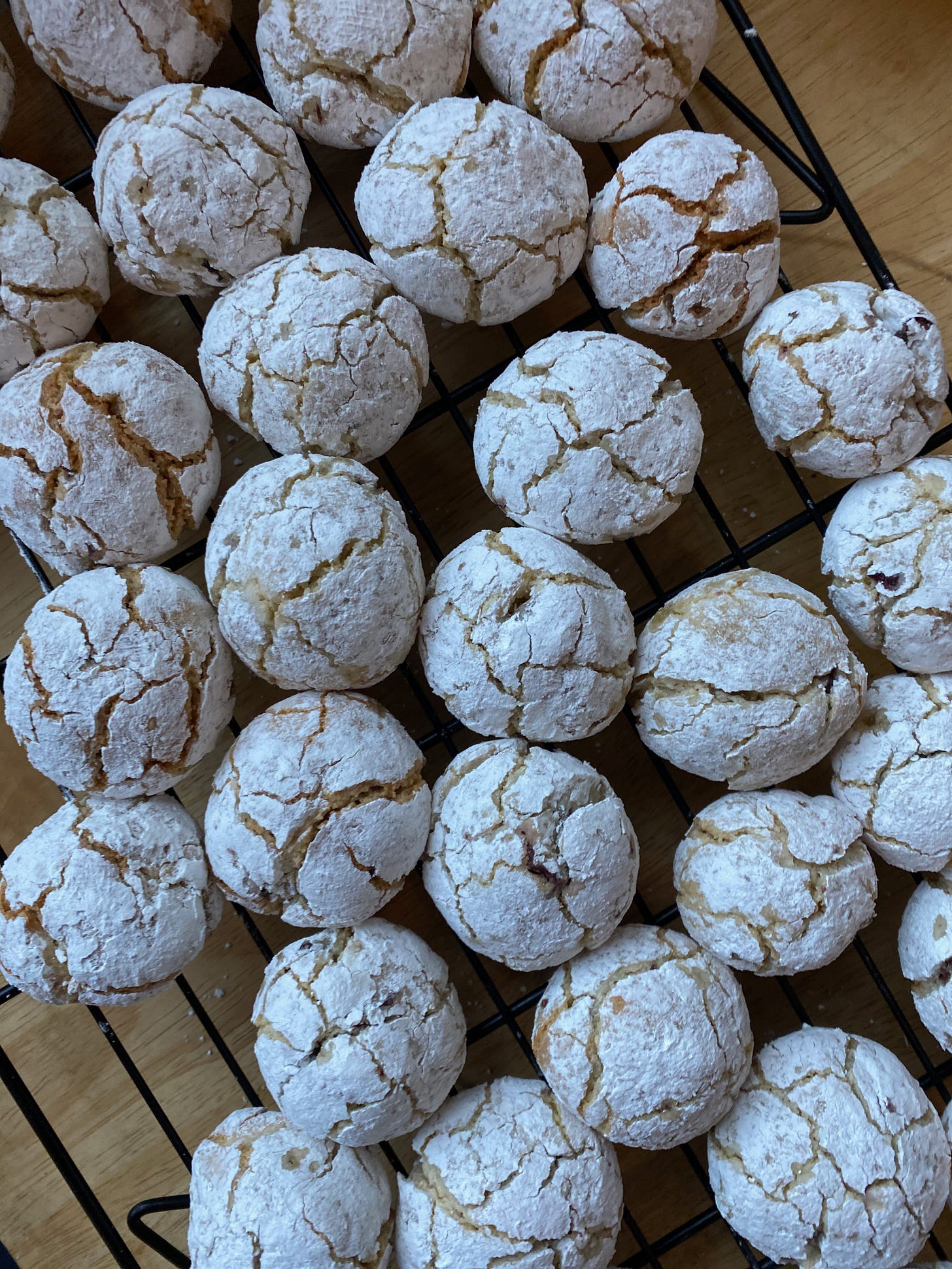 Closeup of many small round cookies, coated in powdered sugar, with uneven cracks all over their tops.