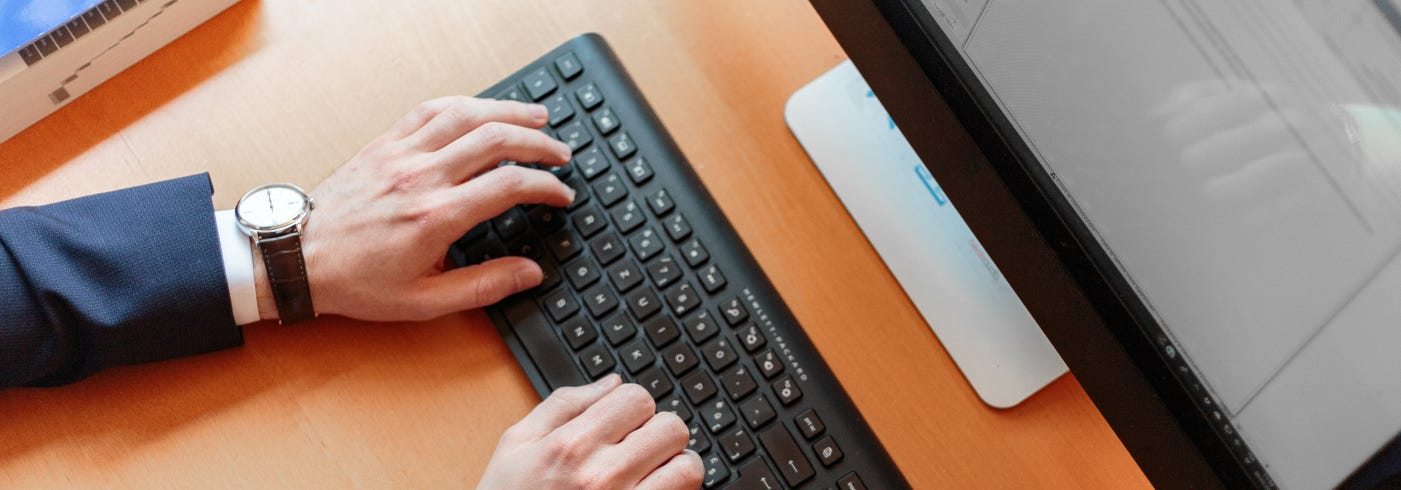 Someone typing in the keyboard on a desk with a computer in front of him