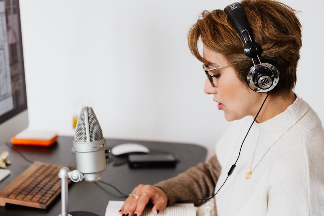 Photo of Woman Reading a Book While Wearing Headphones