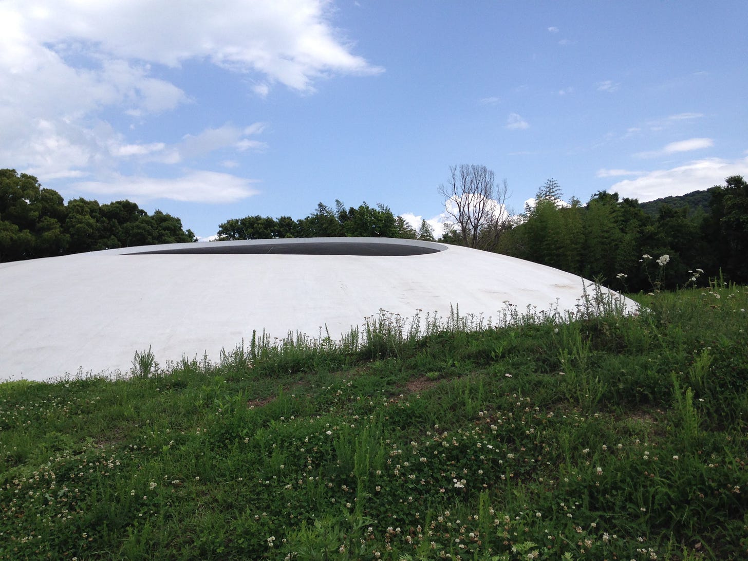 a white domed building with a hole cut out of the top against a blue sky