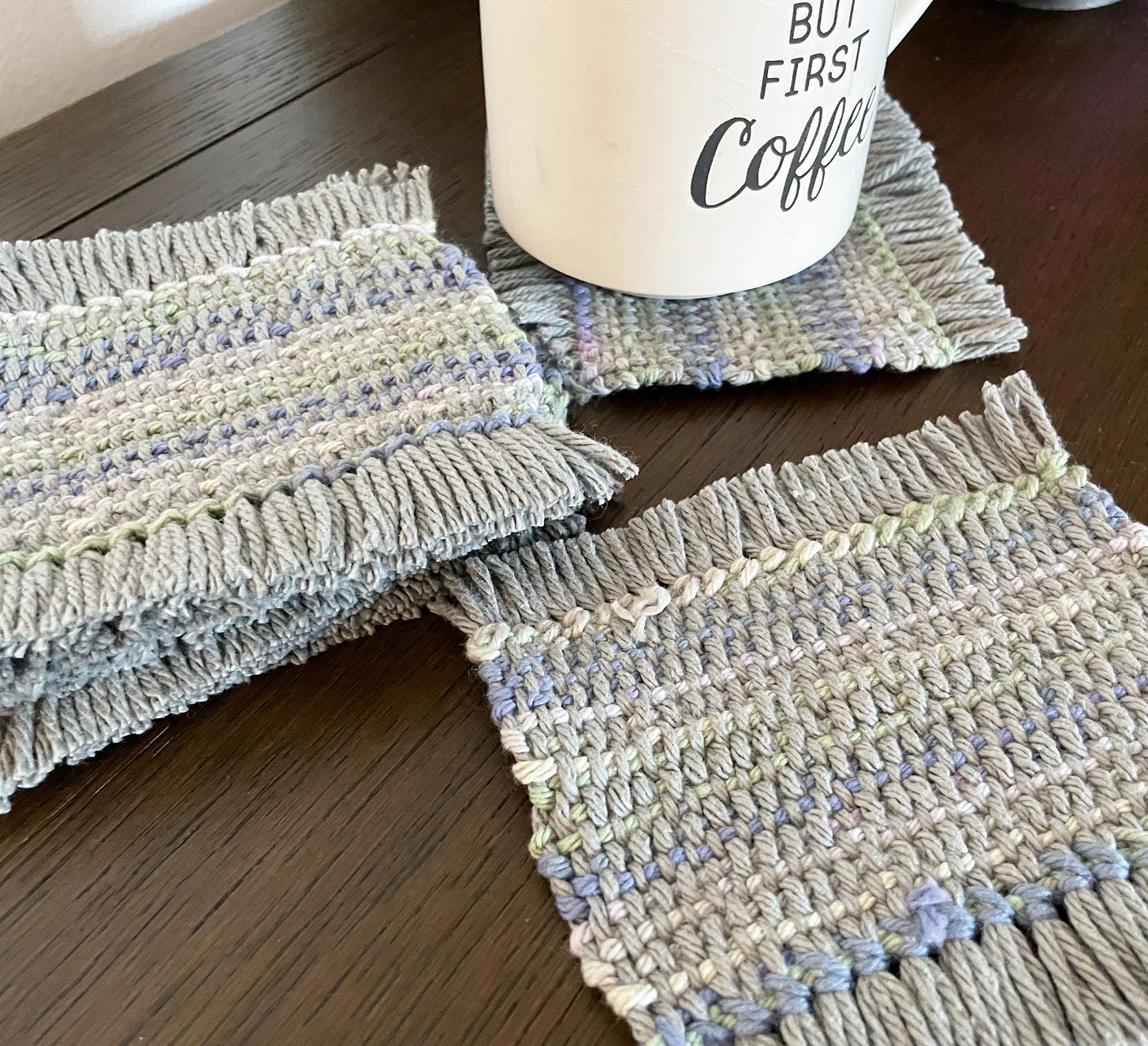 A stack of mug rugs on the left, one in the back with a mug on it, one in the front. Gray and muted colors. No diamonds.