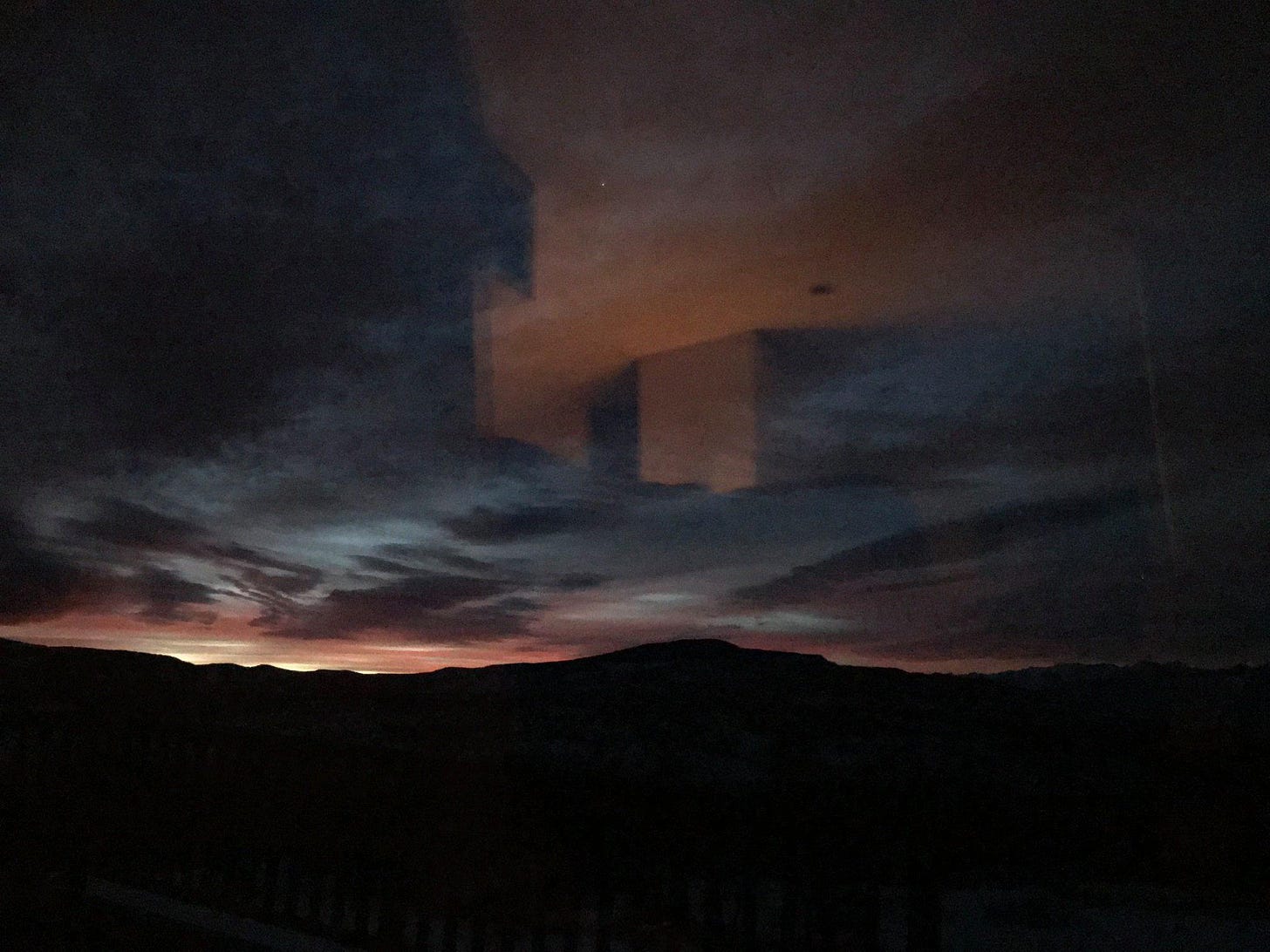 image of early sunrise over distant mountains with some variation in color and a few dark clouds