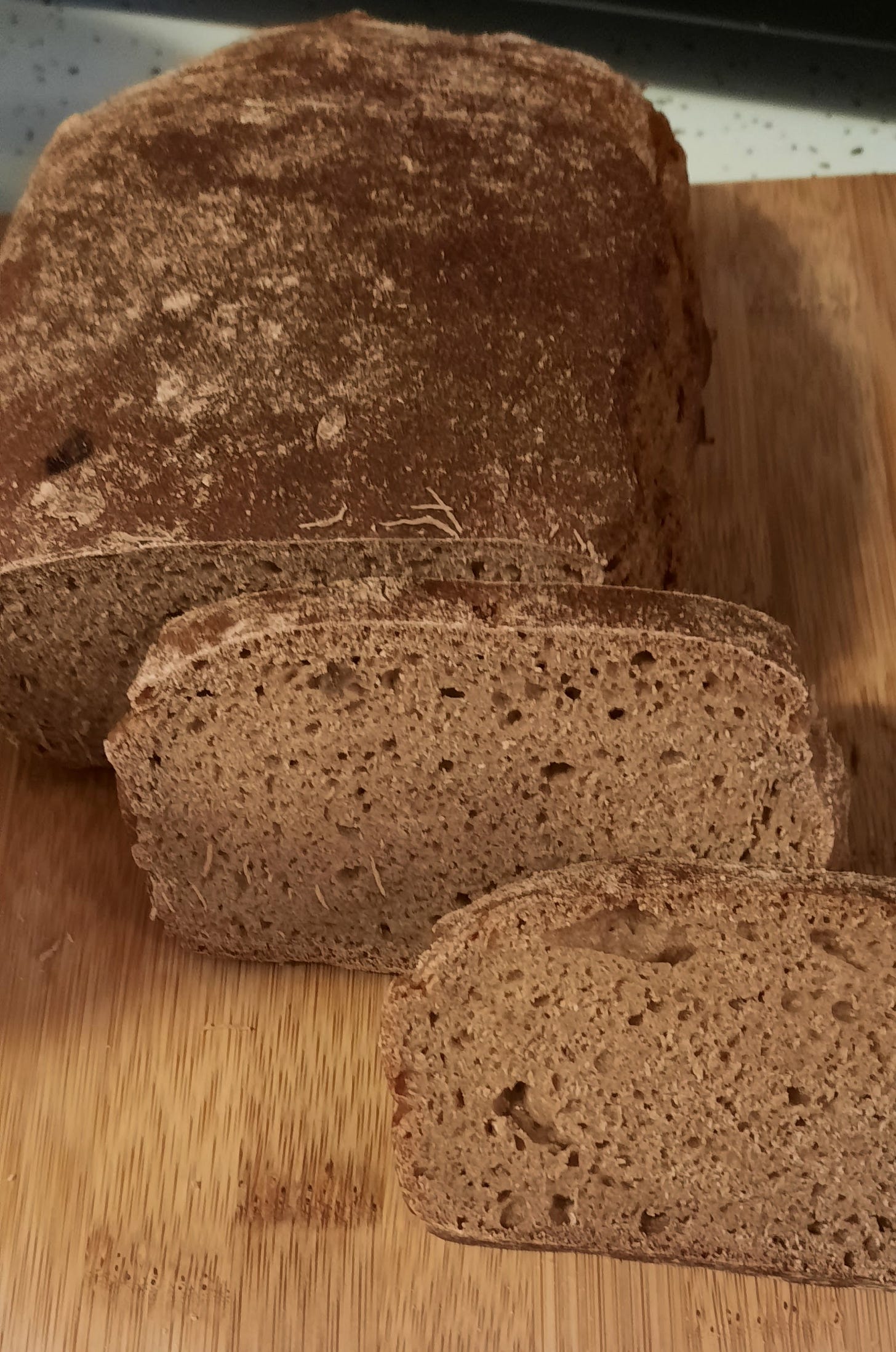 A brown loaf of bread with two slices showing the crumb sit on a brown wooden bread board.