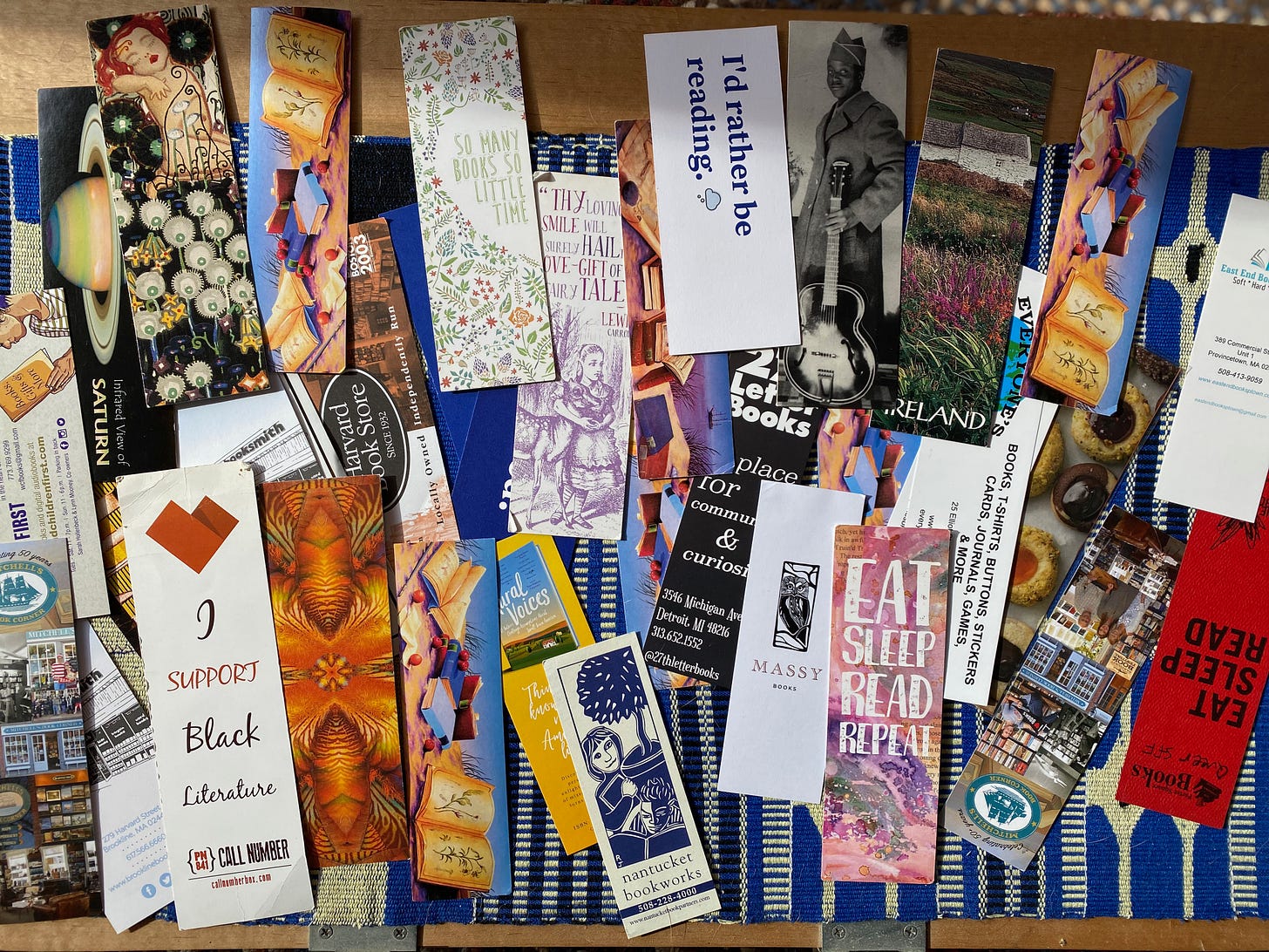 An array of colorful bookmarks spread out over a blue cloth. They come from many different bookstores, and show various words, pictures, and designs. 