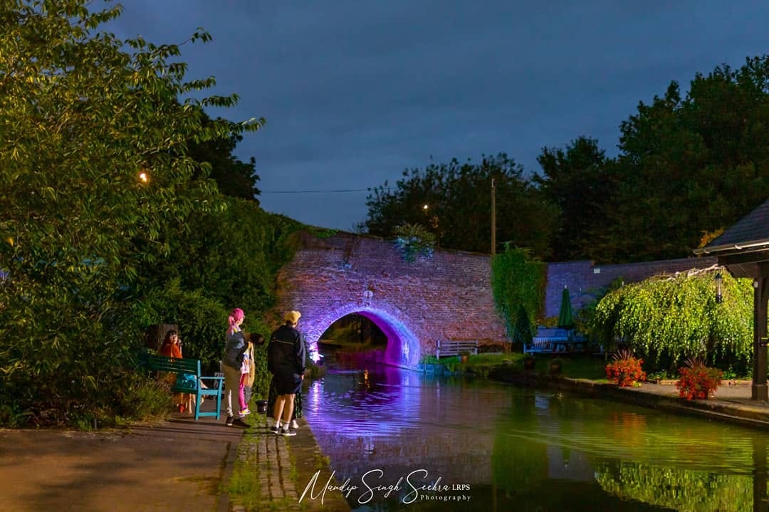 Blue and purple light reflecting off the water beneath a brick bridge to create the illusion of a circle